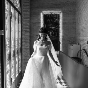 A black and white photo of a bride in an elegant dress indoors.