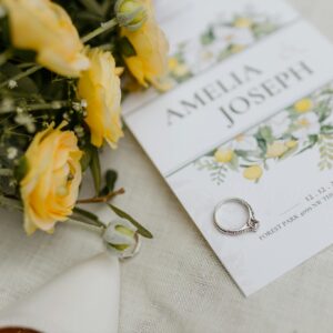 Close-up of wedding invitation adorned with yellow flowers and engagement ring, perfect for elegant wedding themed designs.