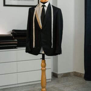 A stylish black suit jacket displayed on a mannequin with a measuring tape, showcasing bespoke tailoring in an elegant studio setting.