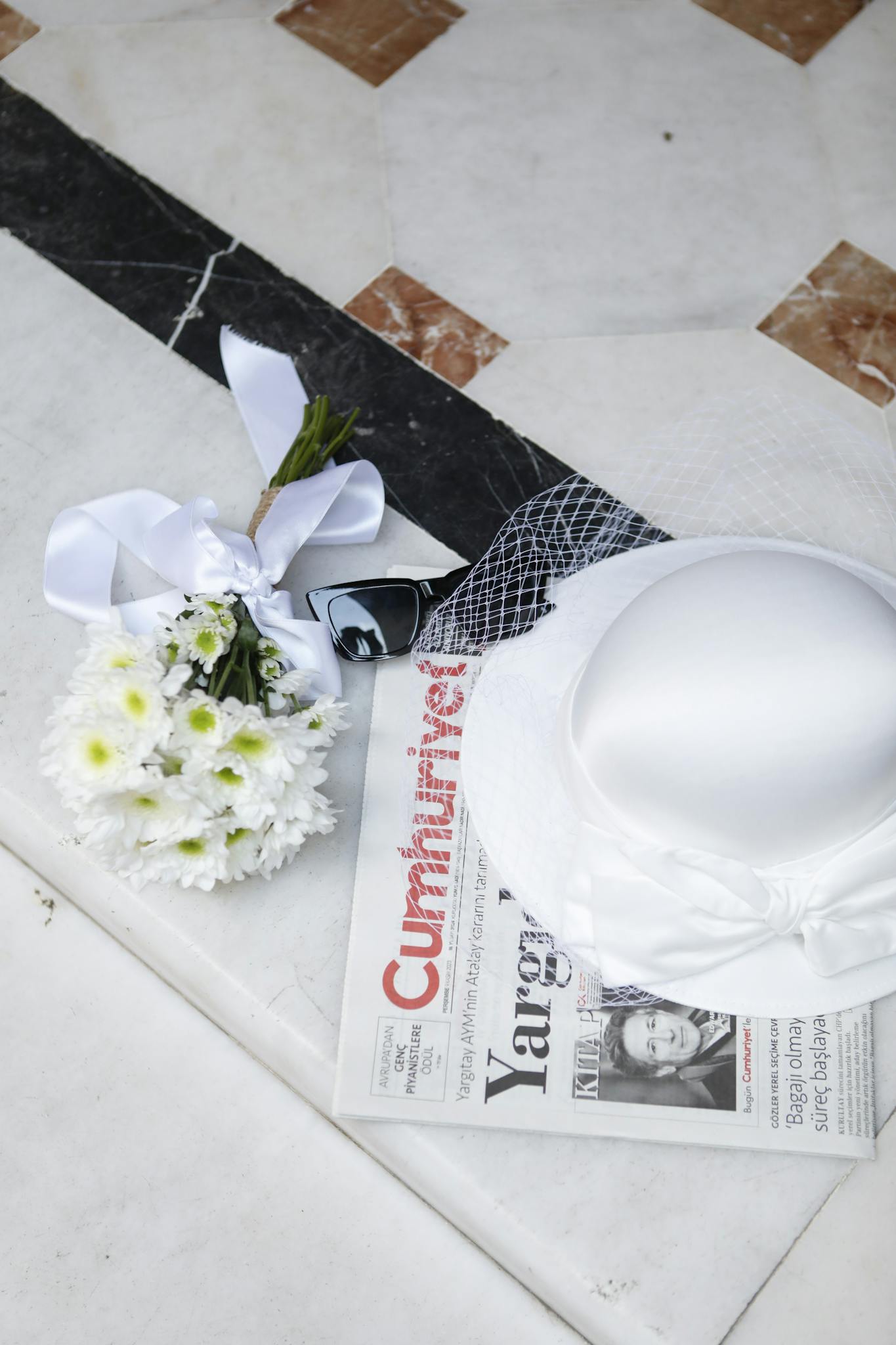 Flat lay of bridal accessories with a white hat and bouquet on a marble floor.