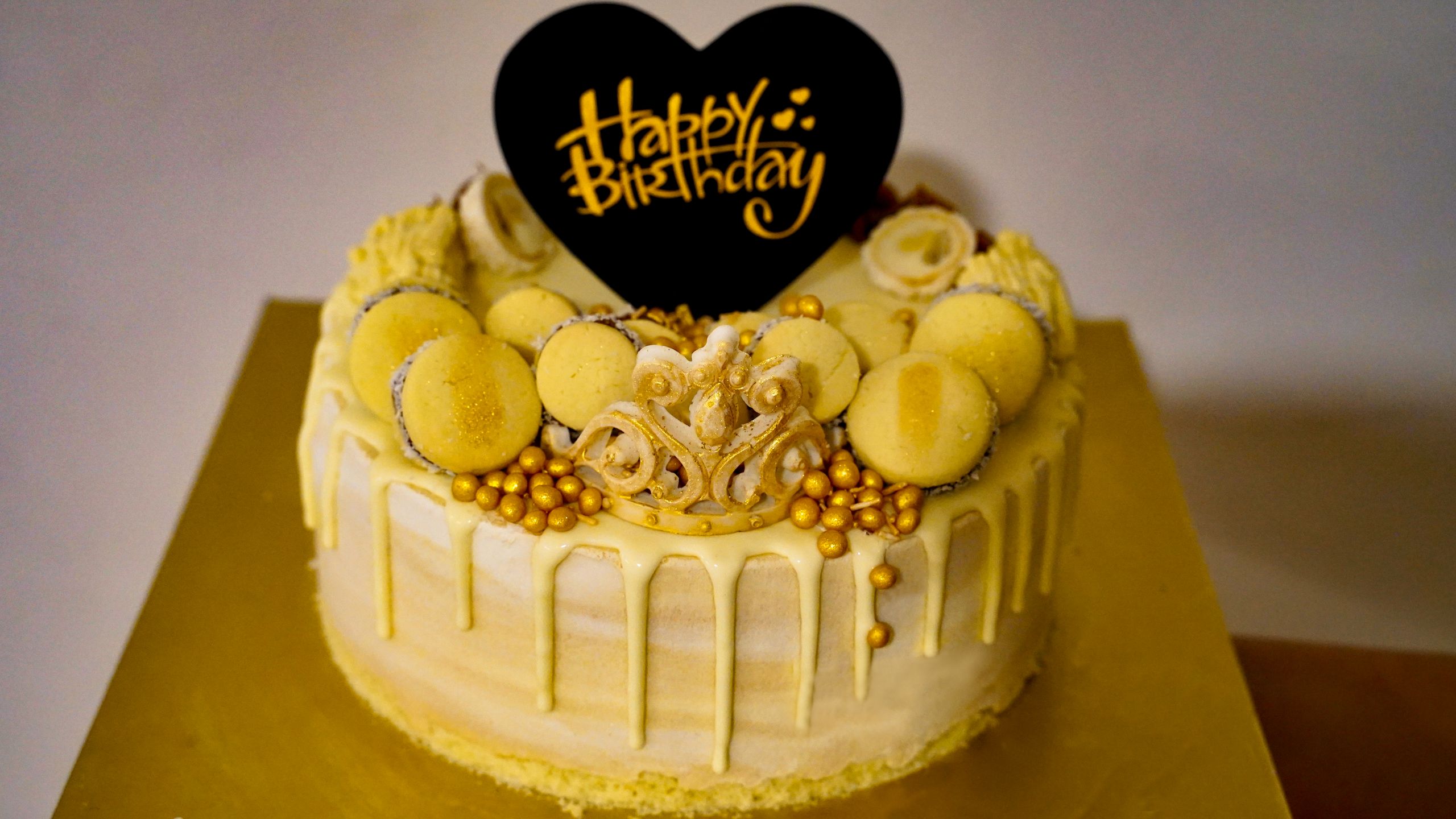 Stylish yellow birthday cake adorned with macarons and golden accents, perfect for celebrations.