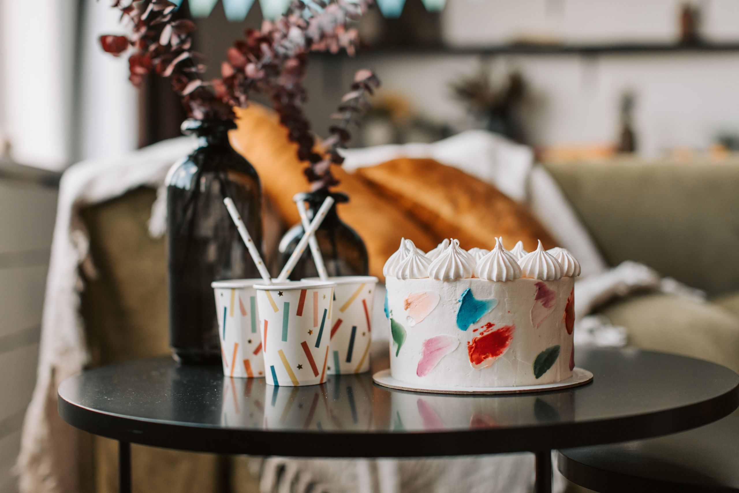 Vibrant cake with decorated cups on a table indoors, creating a cozy and artistic ambiance.