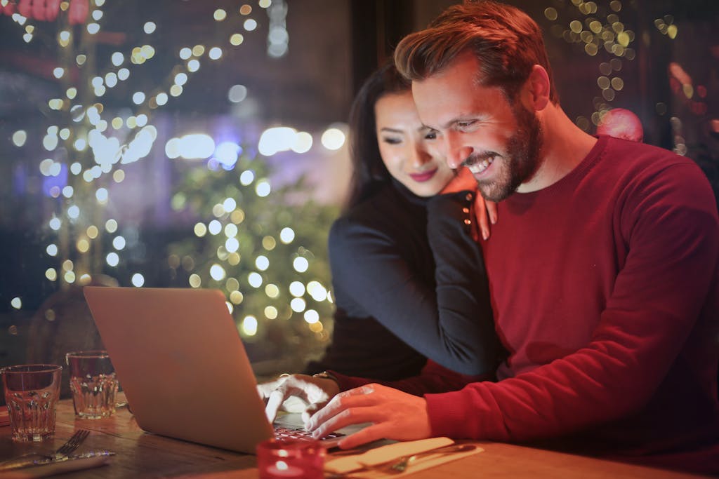A couple using a laptop at a cozy restaurant with festive bokeh lights, enjoying online shopping together.