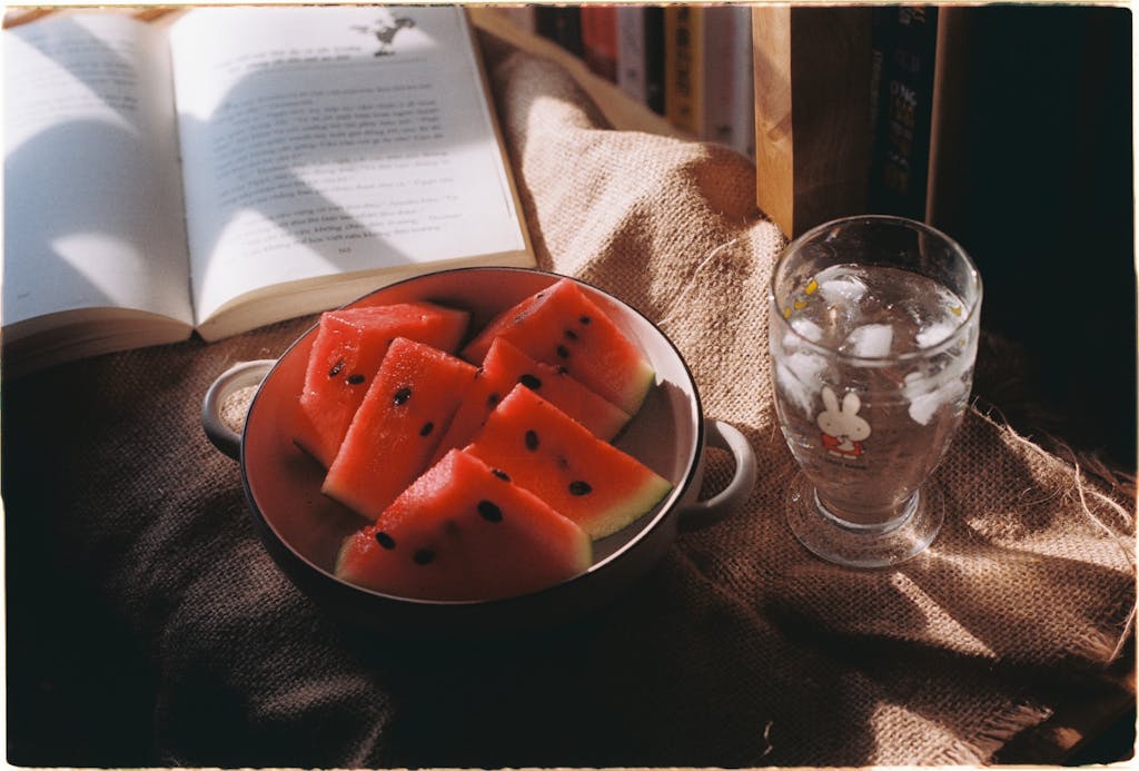 A cozy summer scene with watermelon slices, a refreshing drink, and an open book on a burlap surface.