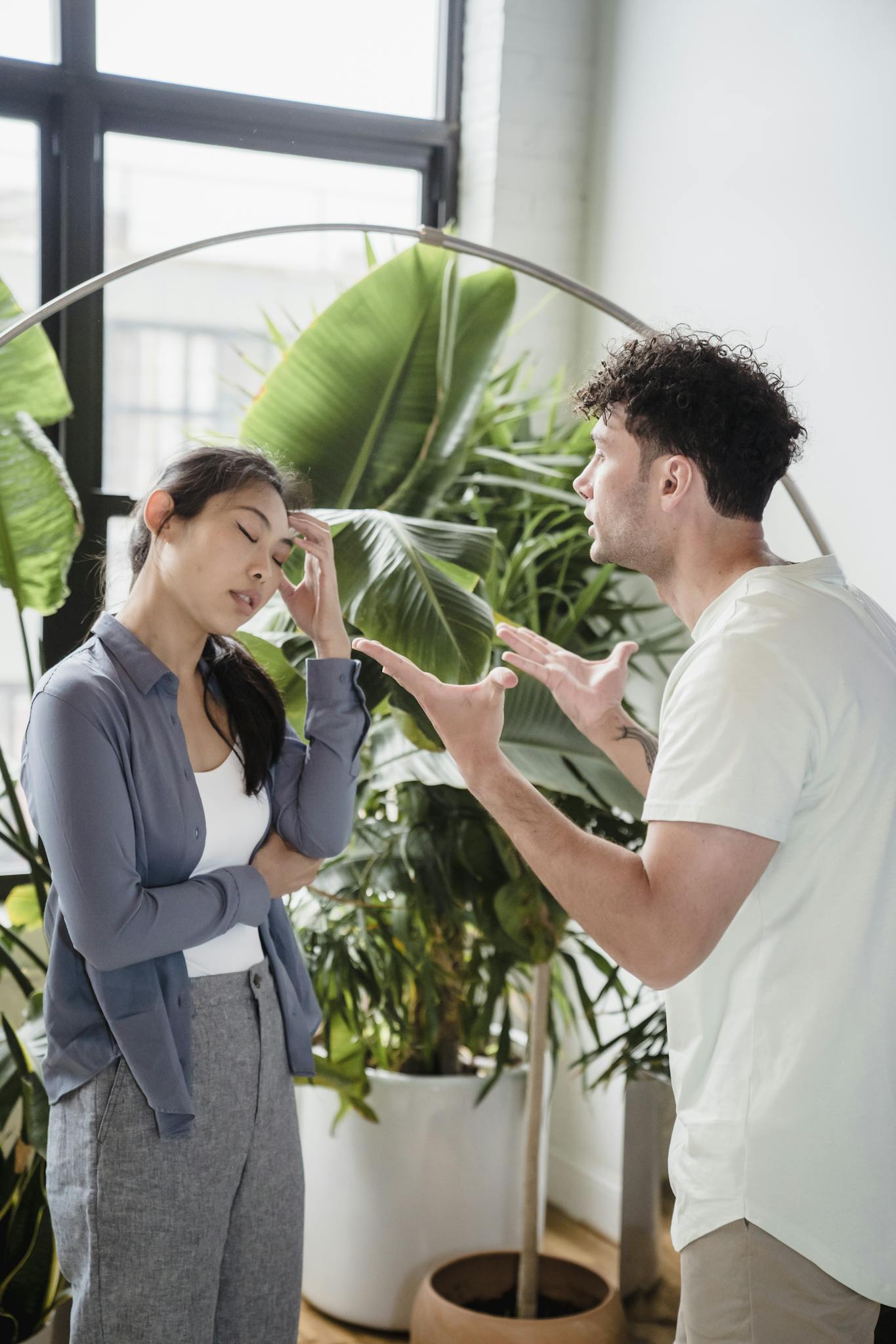 A man and woman having a heated argument indoors, surrounded by plants.