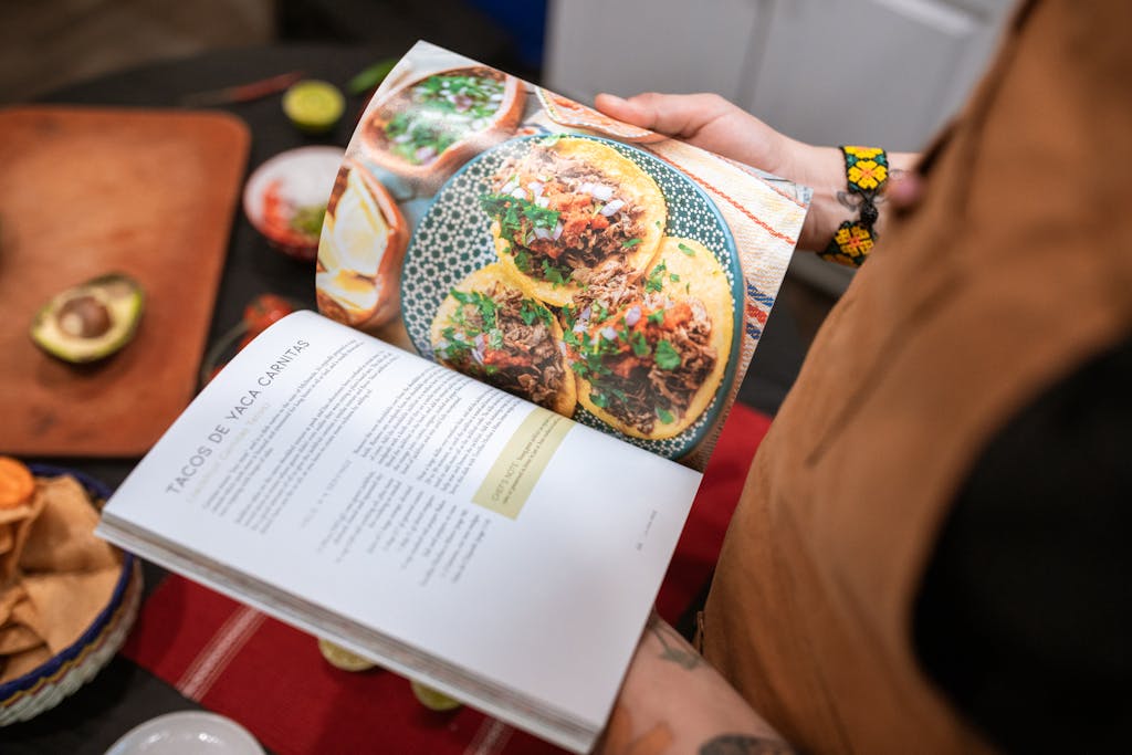 A person holding a cookbook open to a delicious tacos recipe.