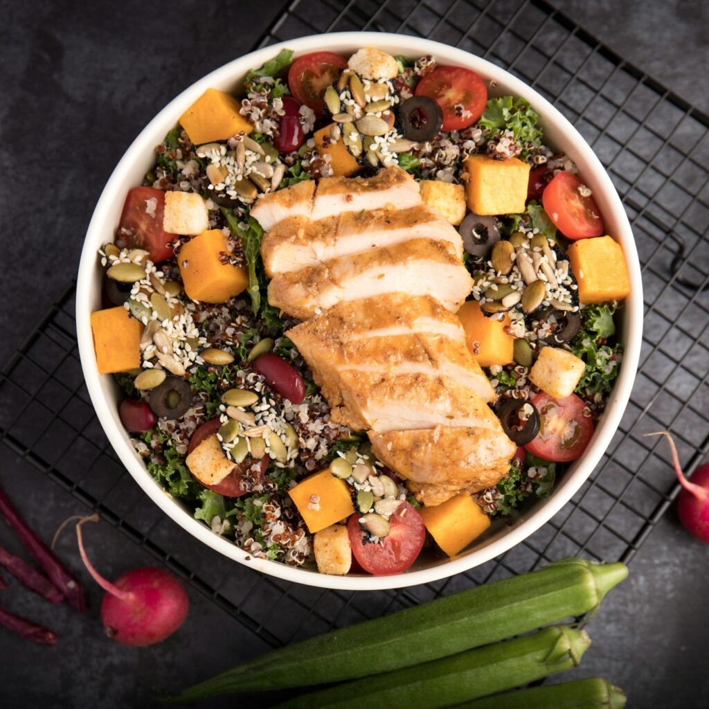 A vibrant bowl of grilled chicken salad with quinoa, fresh vegetables, and seeds.