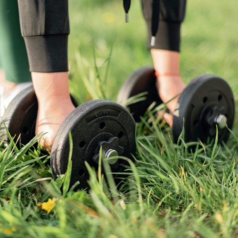 Close-up of a person exercising outdoors with dumbbells on grass, emphasizing fitness and wellness.