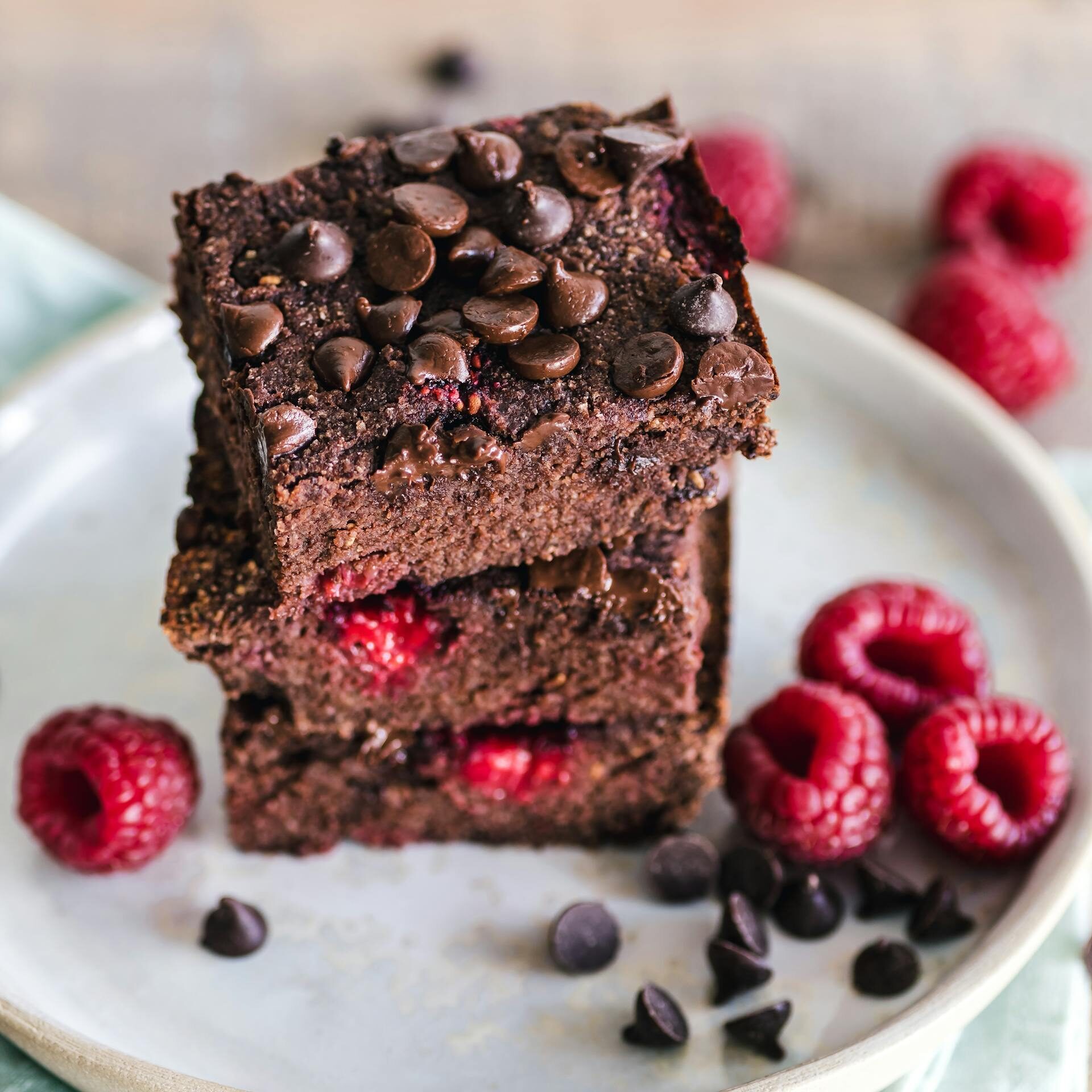 Close-up of deliciously indulgent chocolate raspberry brownies stacked on a ceramic plate with fresh raspberries.