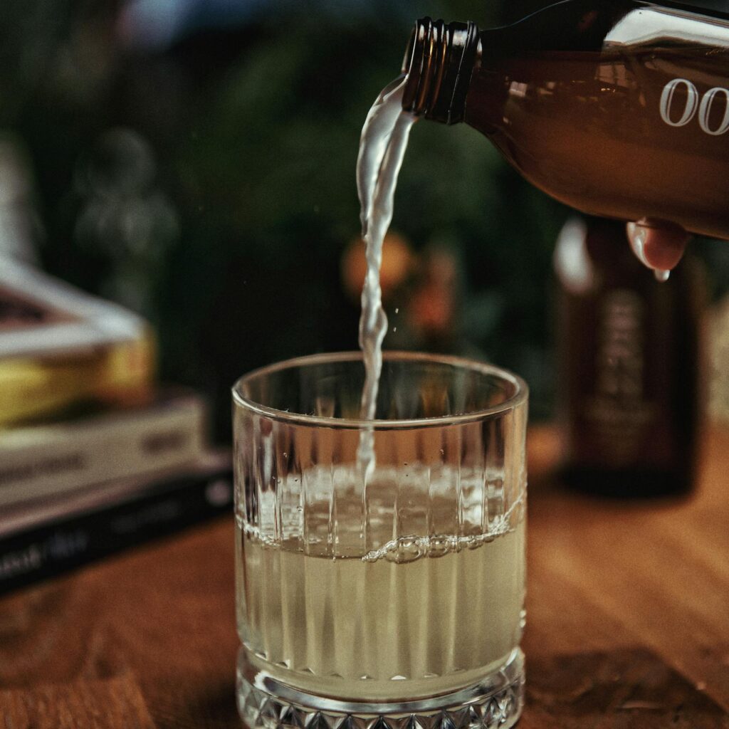 Close-up of kombucha being poured into a crystal glass on a wooden table.