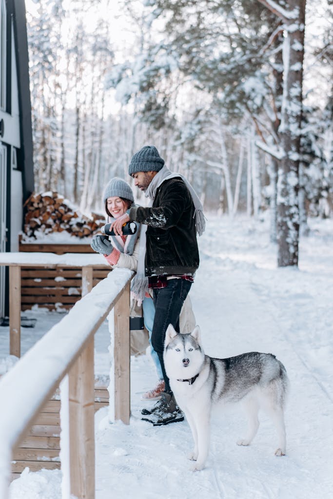 Couple enjoying winter with their Siberian husky at a snowy cabin.