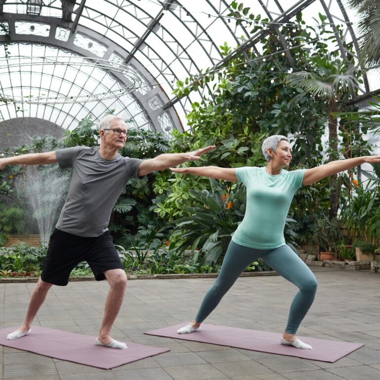 Elderly couple enjoying yoga exercises together in a lush greenhouse setting.