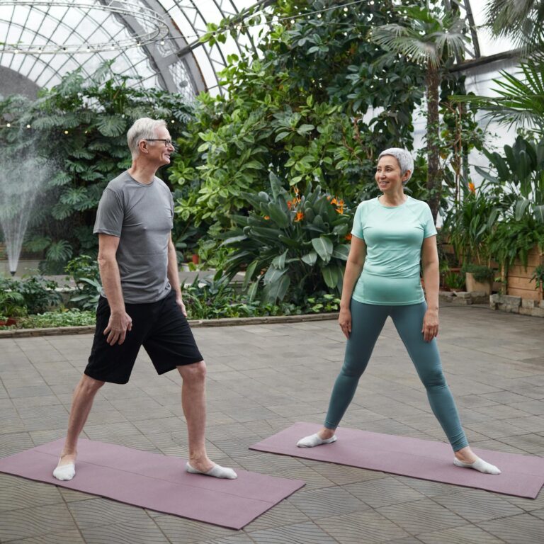 Elderly couple practicing yoga in a lush greenhouse, promoting health and wellness.