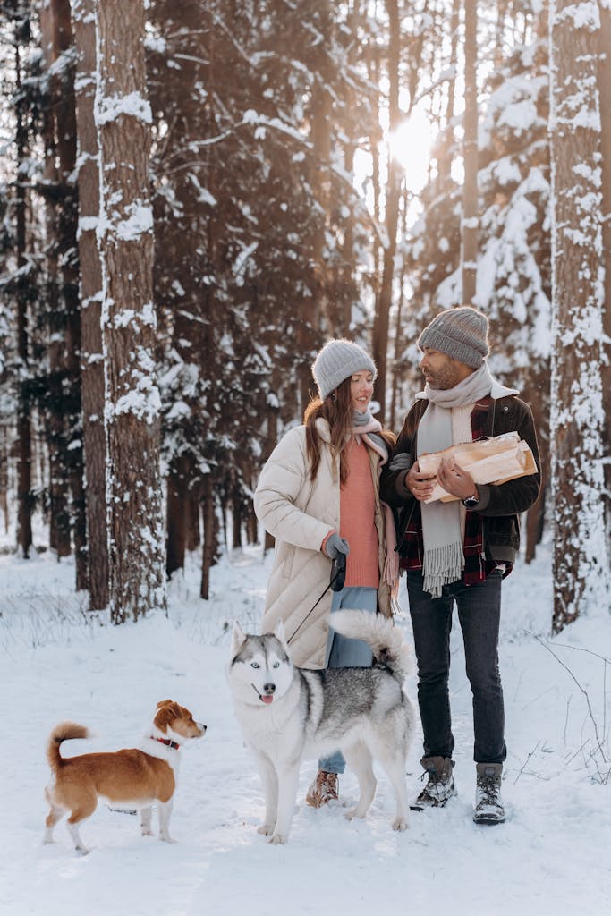 Happy couple walking with dogs in snowy forest, enjoying a winter day outdoors.
