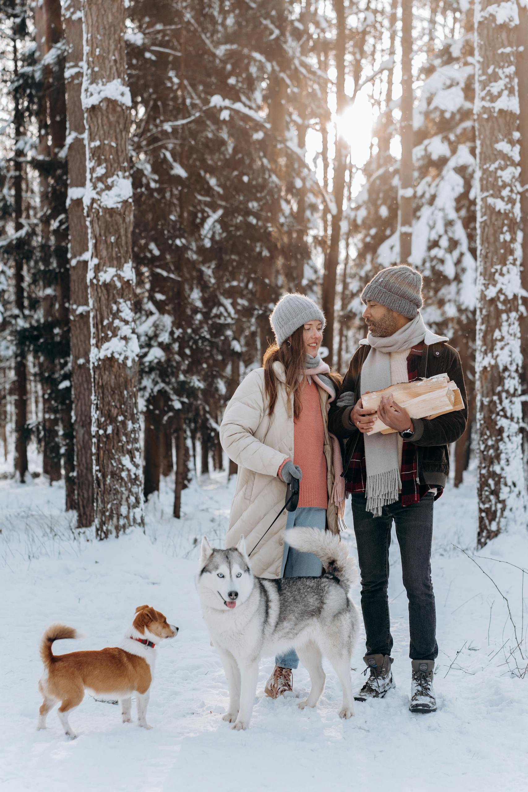 Happy couple walking with dogs in snowy forest, enjoying a winter day outdoors.