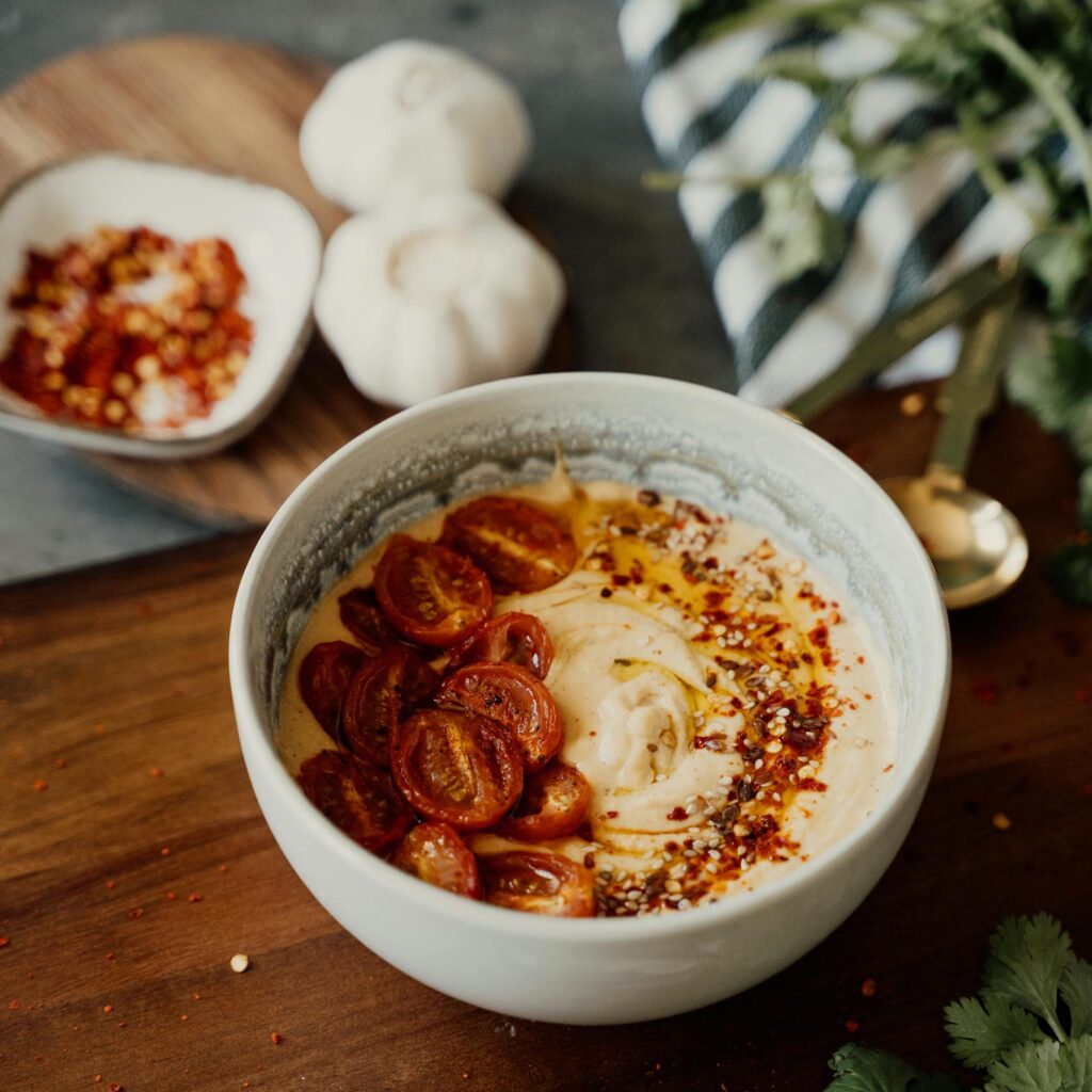 Mouth-watering bowl of hummus topped with fresh cherry tomatoes and spices on a wooden board.