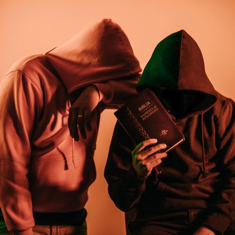 Two hooded figures holding a Bible, conveying mystery and faith.