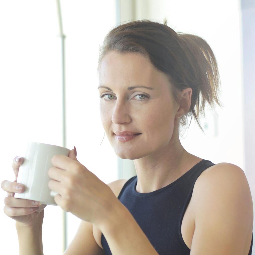 Young woman sitting at her desk, holding a coffee cup and smiling. Ideal for workplace and lifestyle themes.