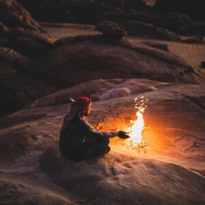 A serene scene of a man sitting by a campfire in the desert landscape of Wadi Rum, Jordan. Photo by Dajana Reçi