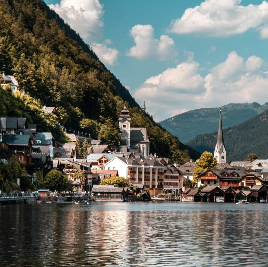 Explore the picturesque town of Hallstatt nestled by a tranquil lake, surrounded by vibrant summer landscapes and majestic mountains.