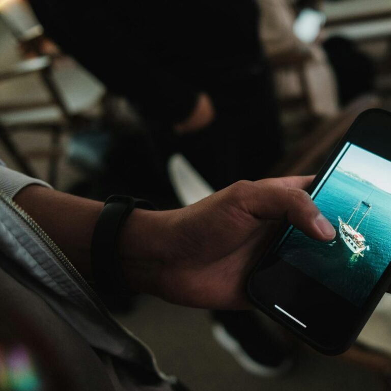 Hand holding a smartphone displaying a yacht photo, perfect travel inspiration.