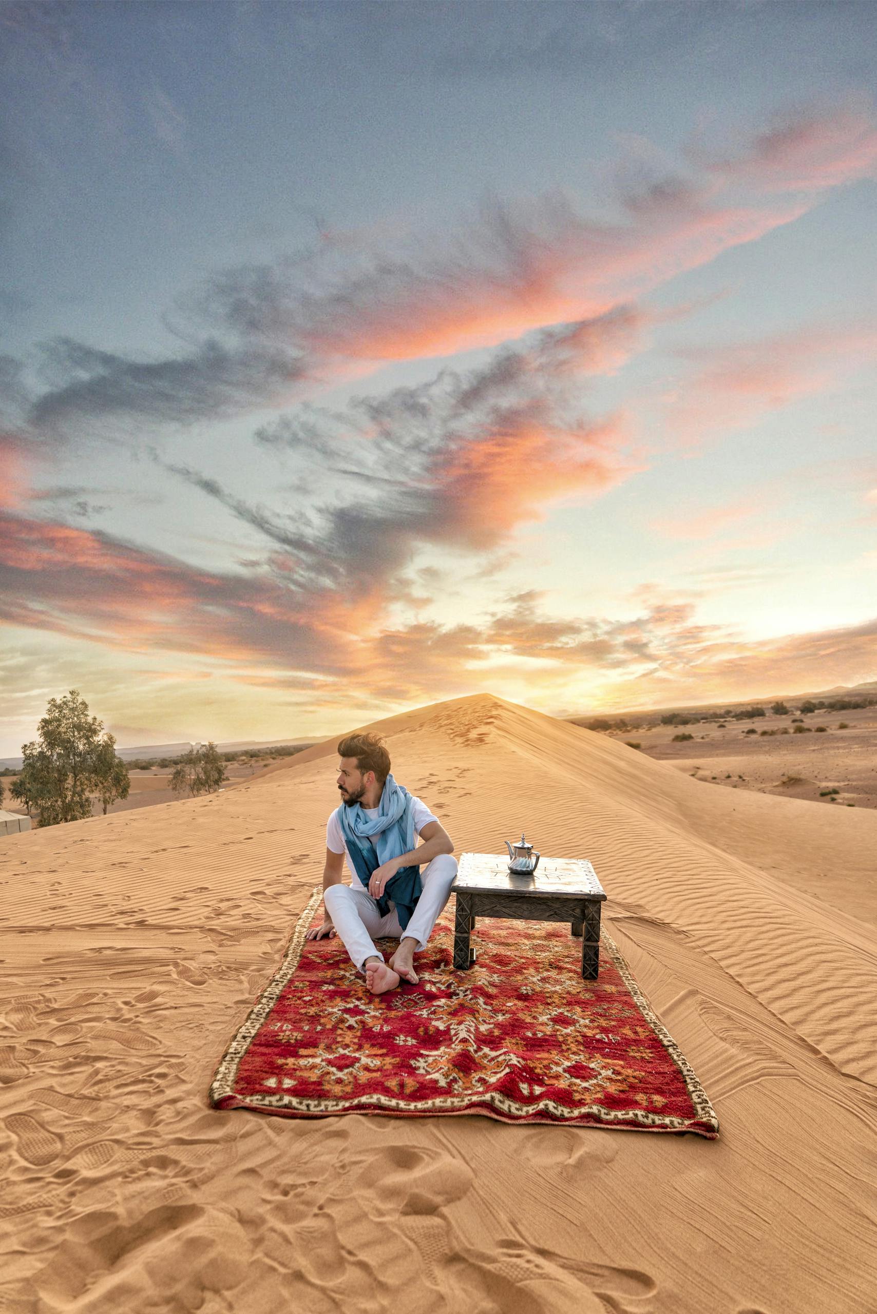 Serene image of a person relaxing on a carpet in the Moroccan desert at sunrise. Photo by Zakaria Boumliha