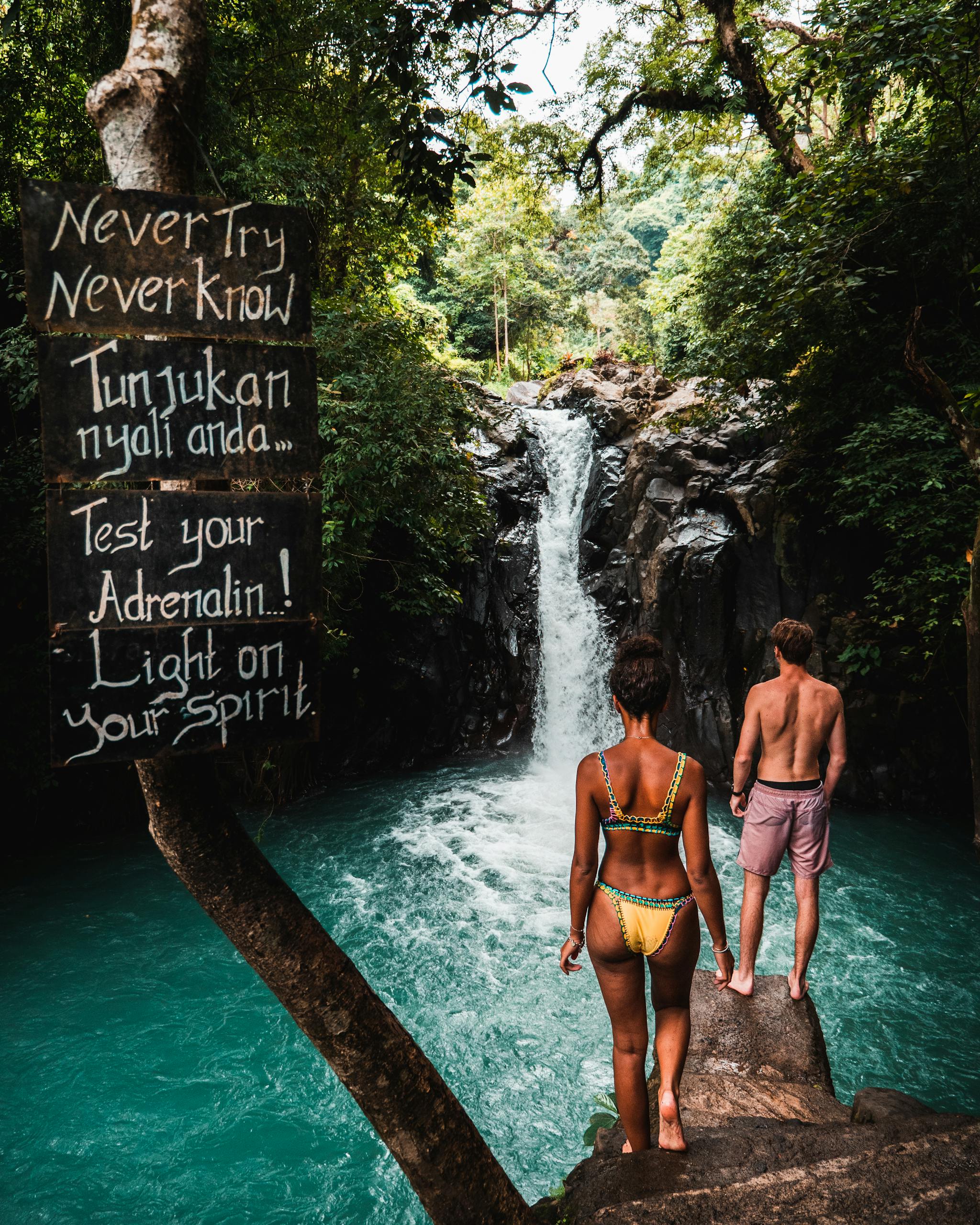 A couple stands before a stunning waterfall in Bali, embracing adventure and nature.