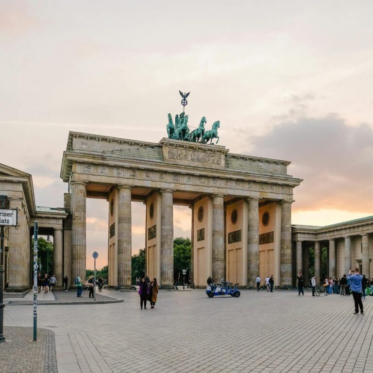 Scenic view of Berlin's Brandenburg Gate with people gathering at sunset.
