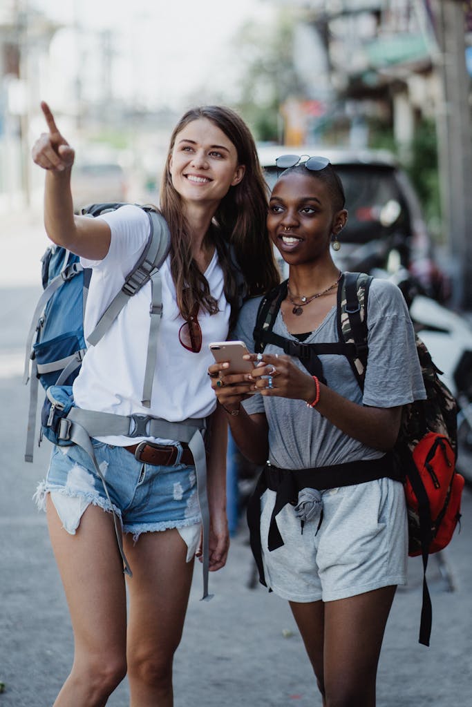 Two smiling women enjoying a day of sightseeing in an urban area, pointing and using a smartphone to navigate.