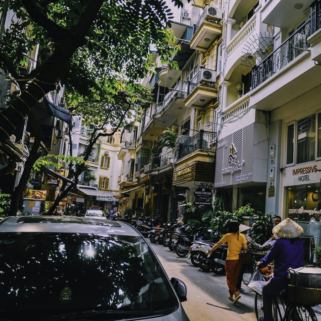 Vibrant street life in Hanoi with locals, cafes, and motorbikes on a sunny day.
