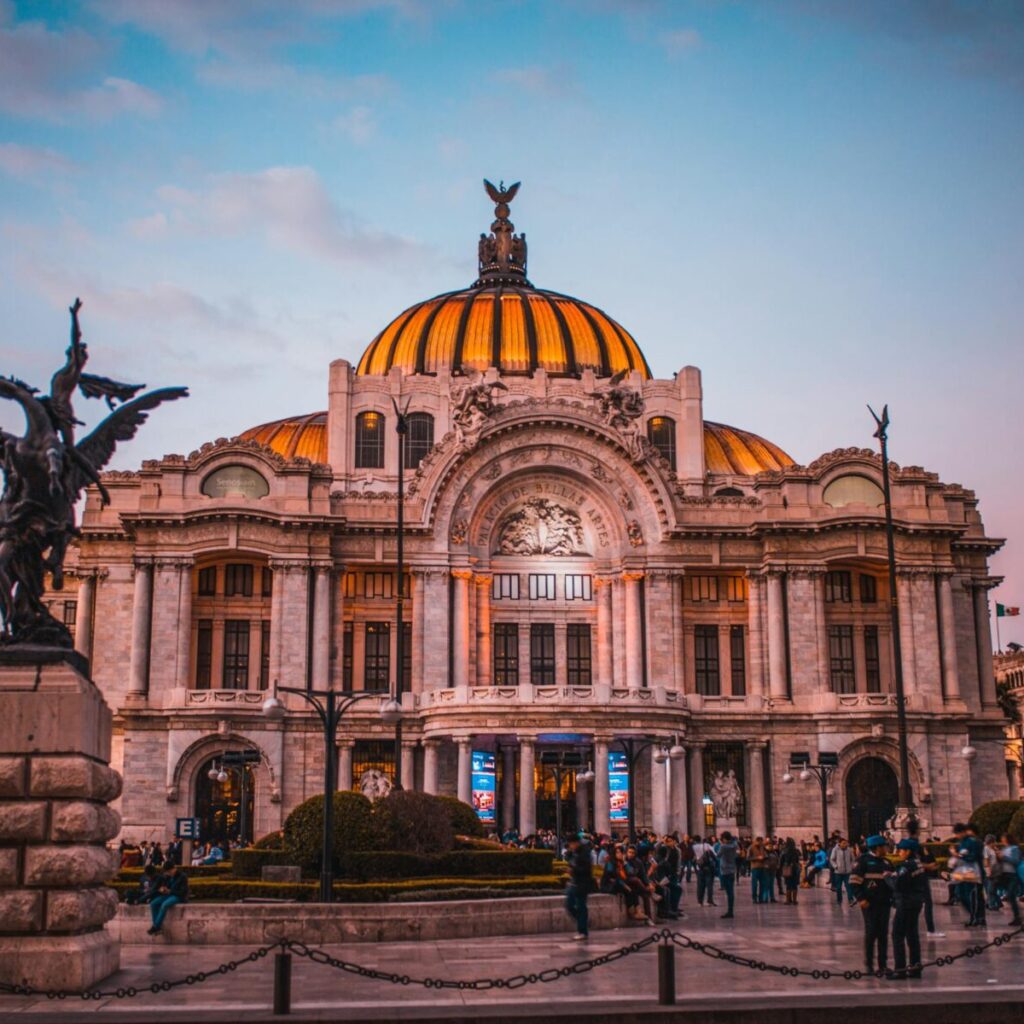 Vibrant sunset at the historic Palacio de Bellas Artes in Mexico City, bustling with tourists.