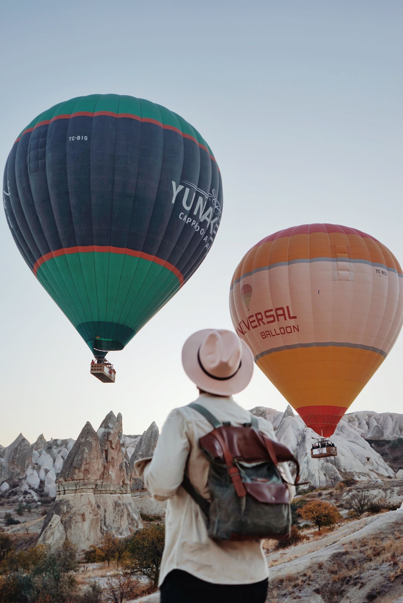 A traveler watches vibrant hot air balloons rise over Cappadocia's unique rock formations.