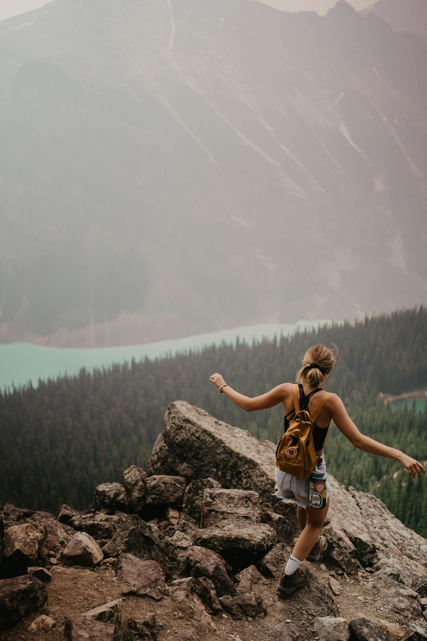 An adventurous woman hikes a rocky trail overlooking a stunning mountain lake view.