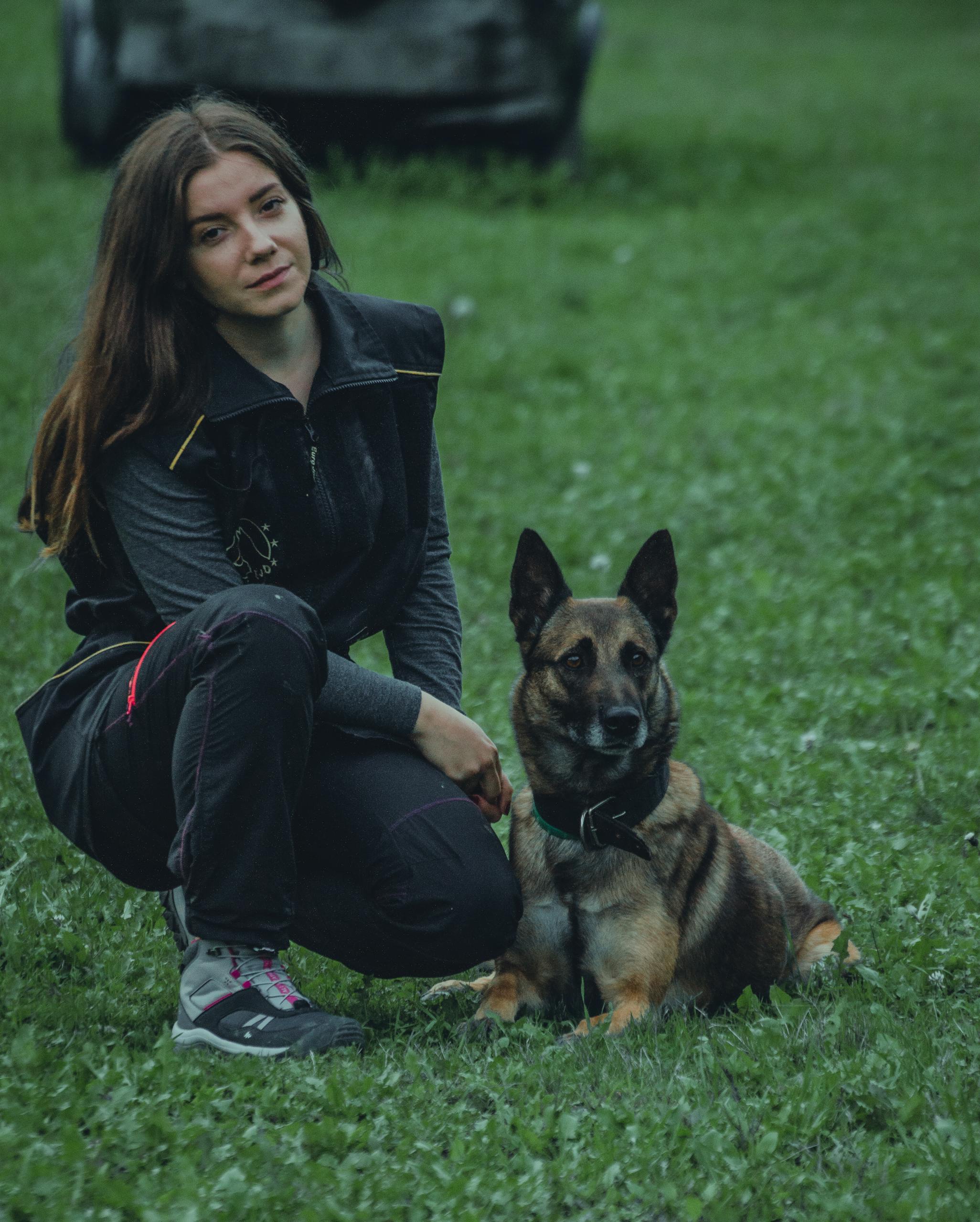 A woman kneels beside her German Shepherd dog on a green lawn, creating a serene outdoor moment.