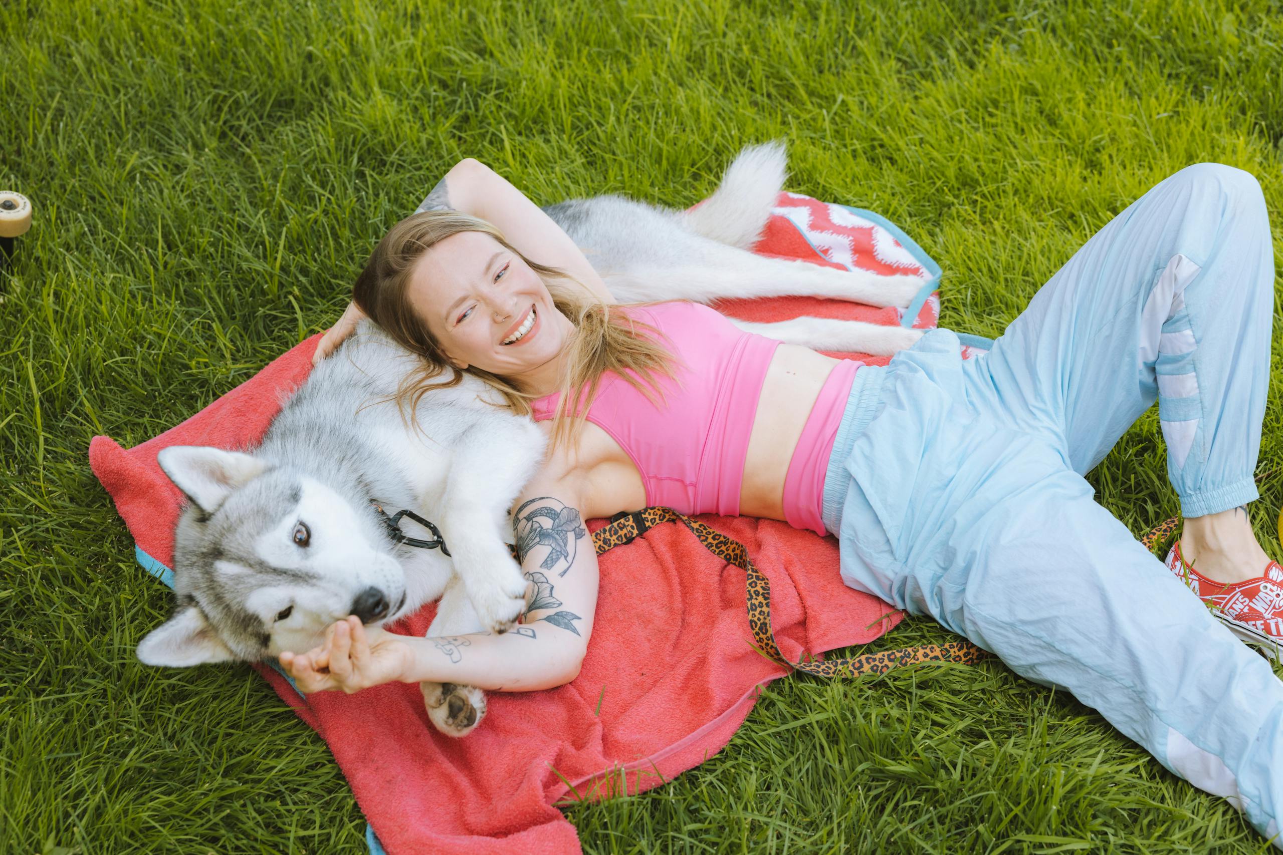 A woman relaxes on a blanket with her Siberian husky in a sunny park, showcasing a bond of friendship.