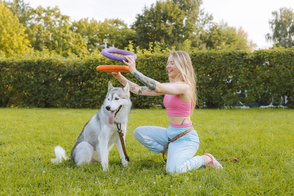 Woman enjoying a playful moment with her husky dog outdoors in a sunny park setting.