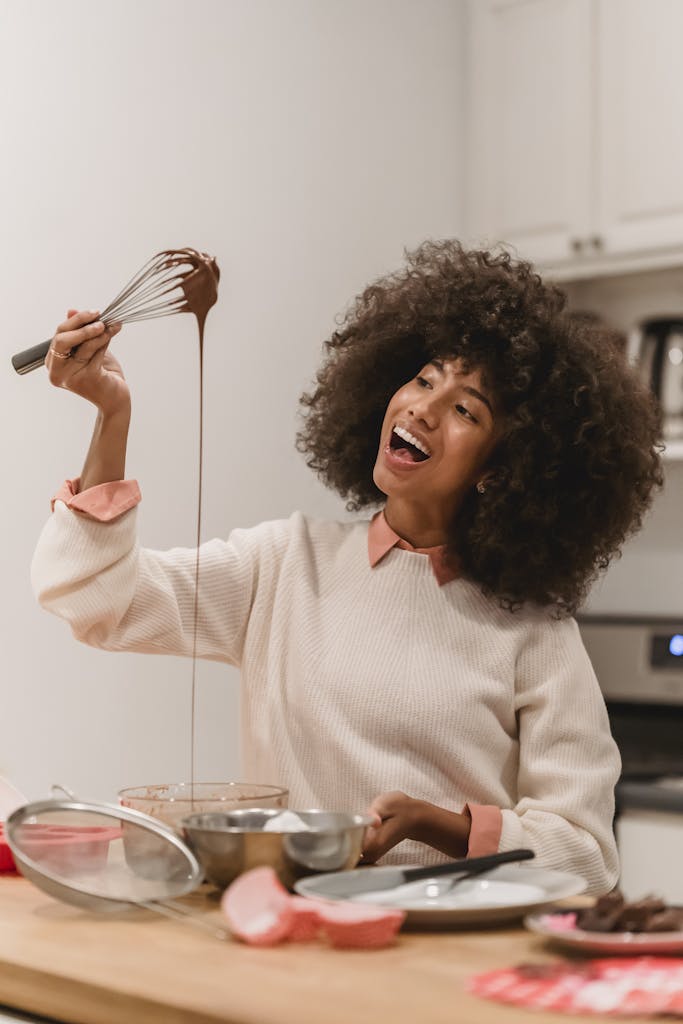 A cheerful woman in the kitchen whisking chocolate with happiness and joy.