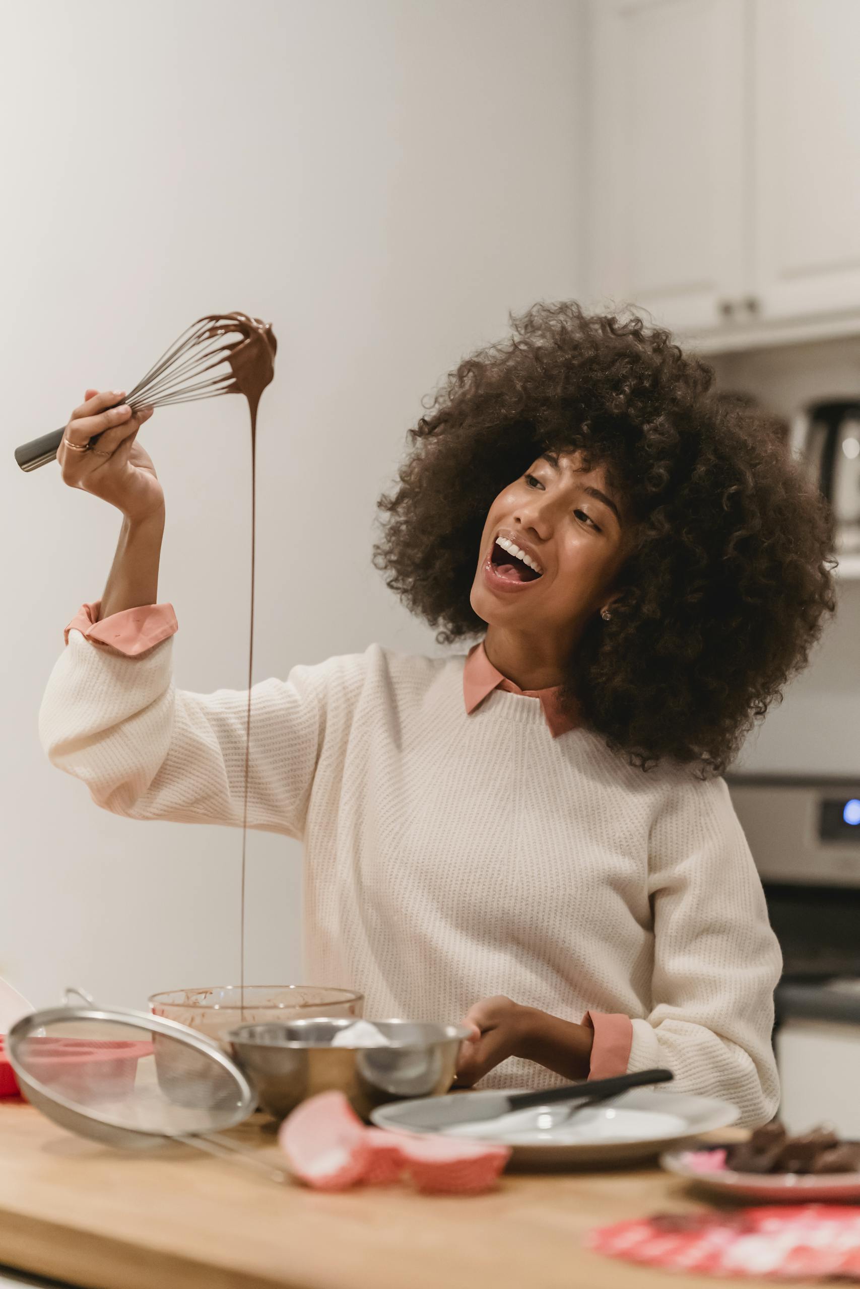 A cheerful woman in the kitchen whisking chocolate with happiness and joy.