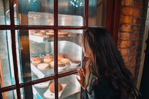 A woman gazes intently at a variety of delicious pastries through a bakery window.
