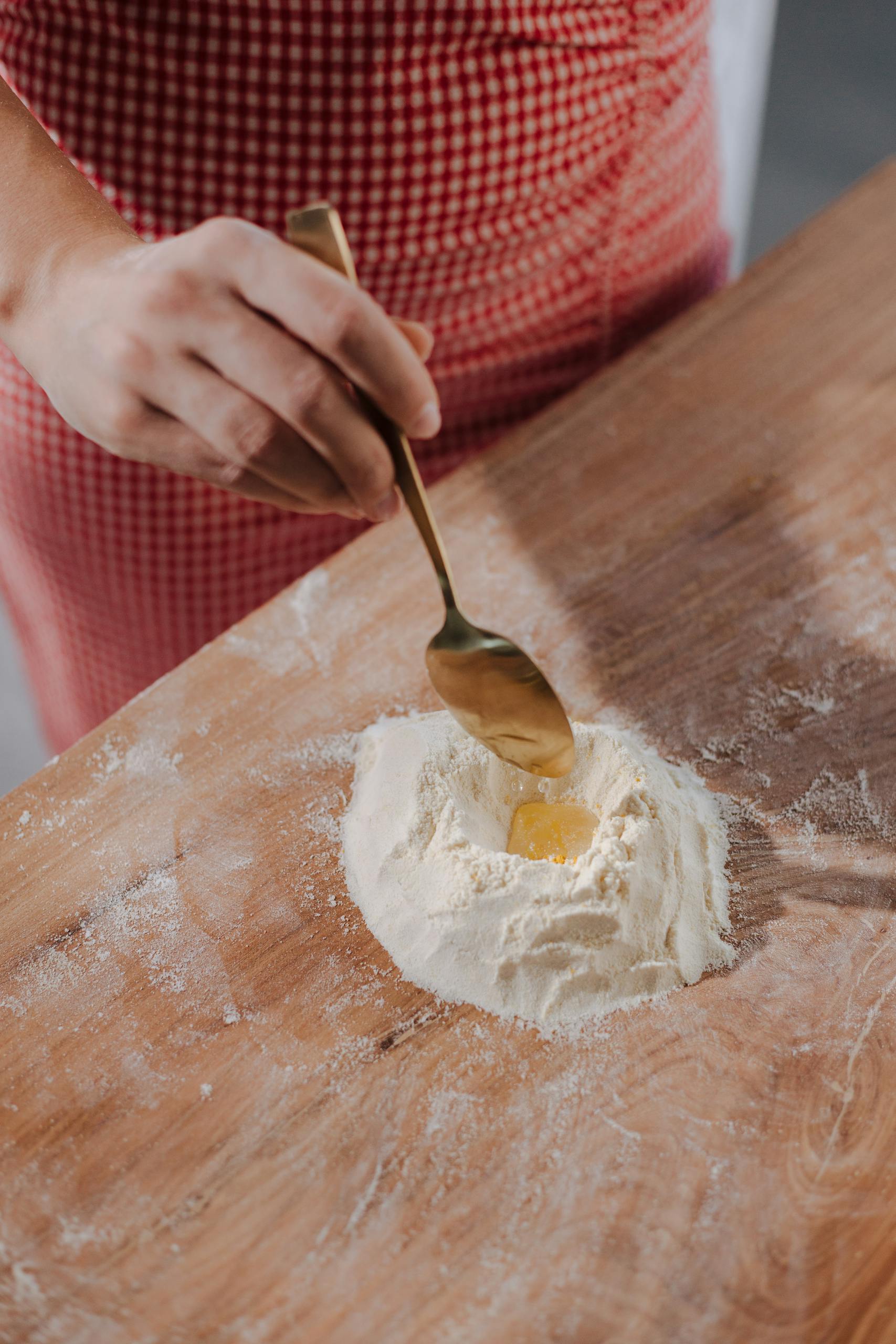 Close-up of a person mixing flour and egg with a spoon on a wooden surface.