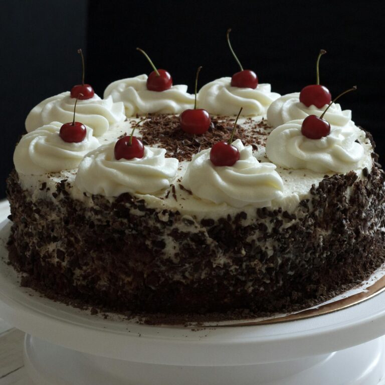 Delicious Black Forest cake topped with whipped cream and cherries on a cake stand.