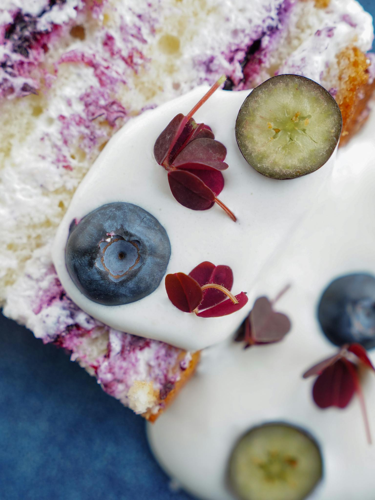 Detailed close-up of a blueberry cake slice topped with yogurt and garnished with fresh blueberries.
