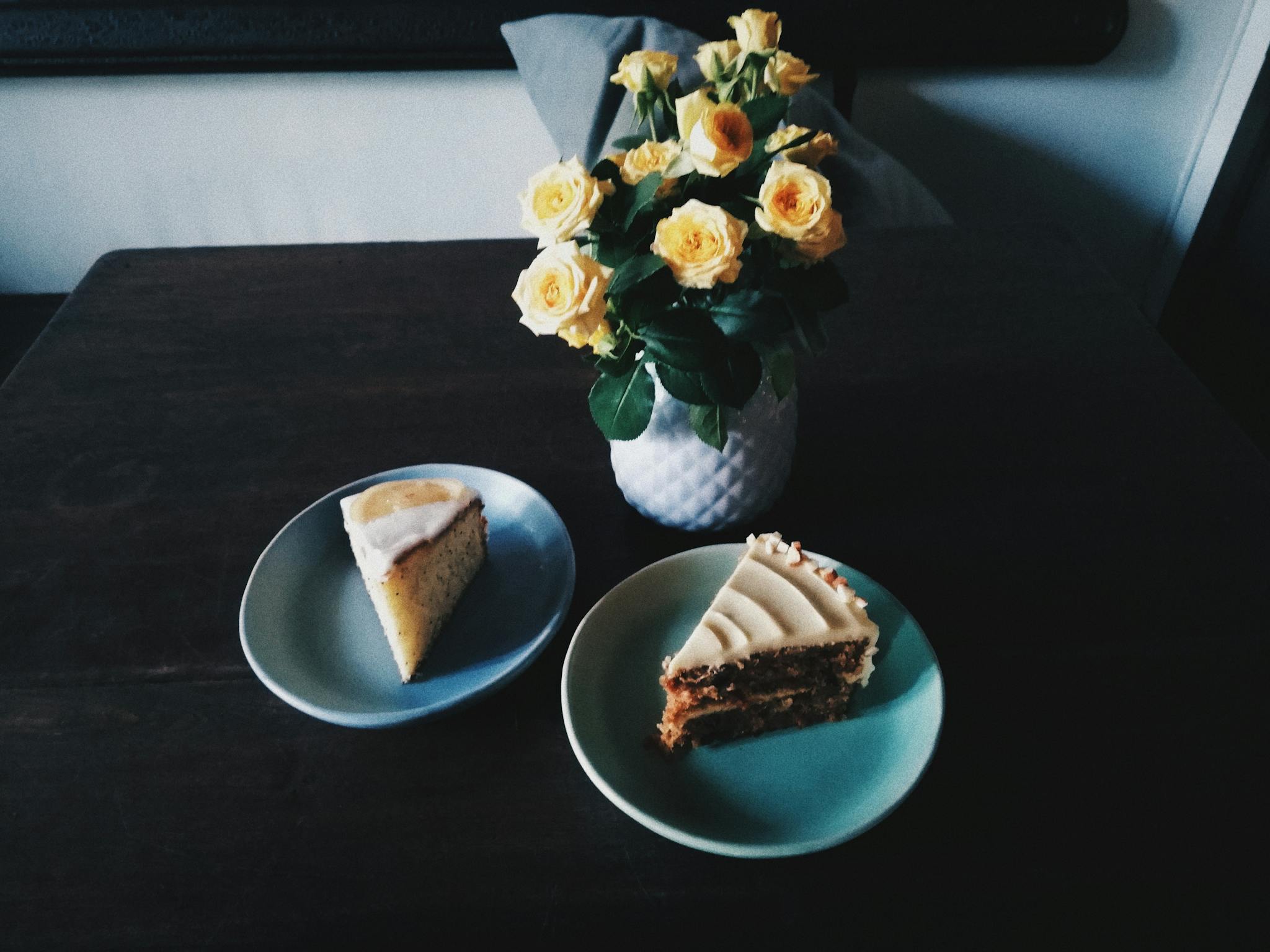Indulgent slices of cake accompanied by a bouquet of yellow roses in a cozy indoor setting.