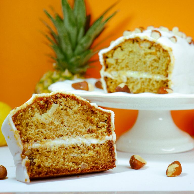 Sliced pineapple and almond cake displayed on a cake stand with vibrant orange background.