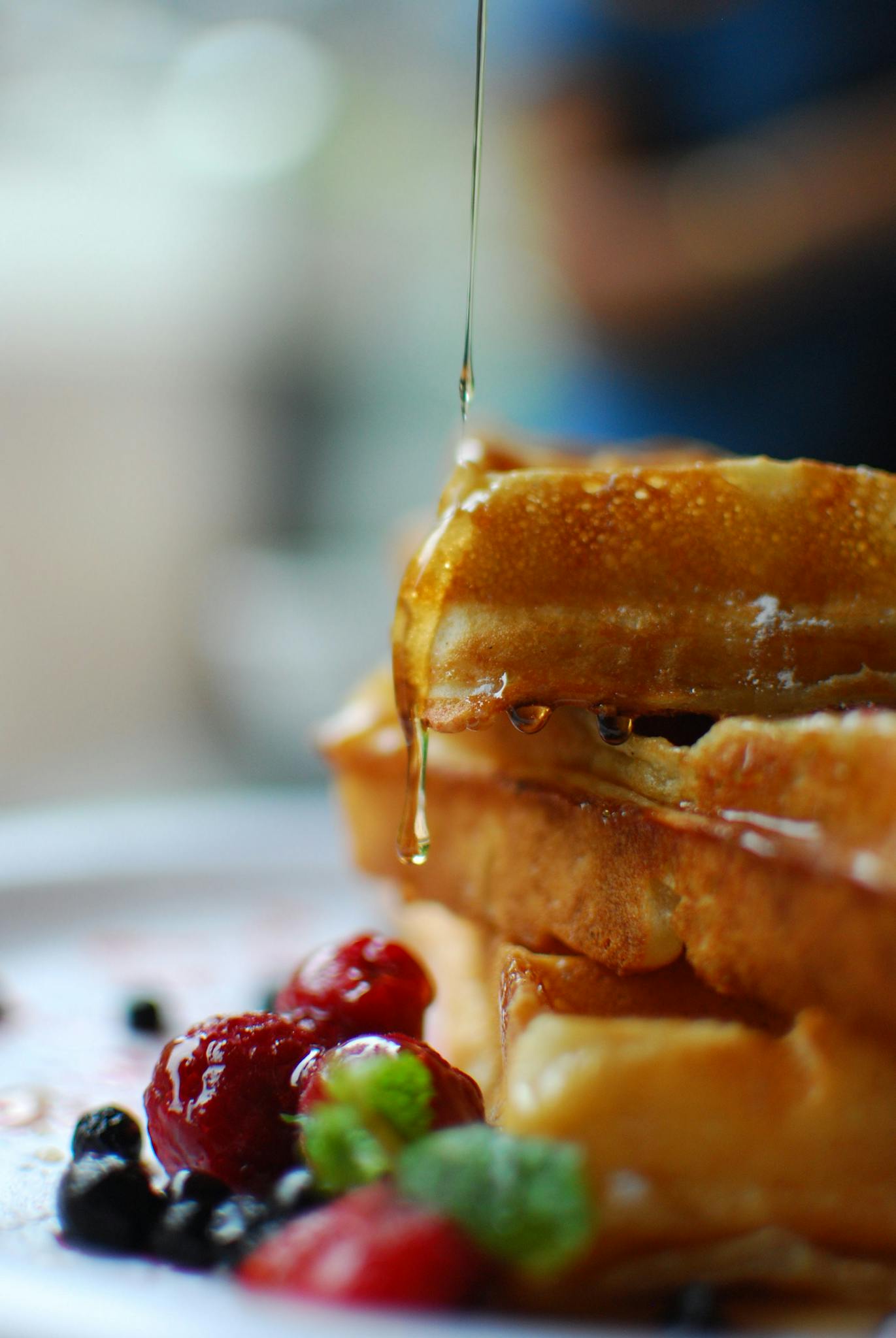 Syrup drips onto stacked waffles with fresh berries, a breakfast delight.
