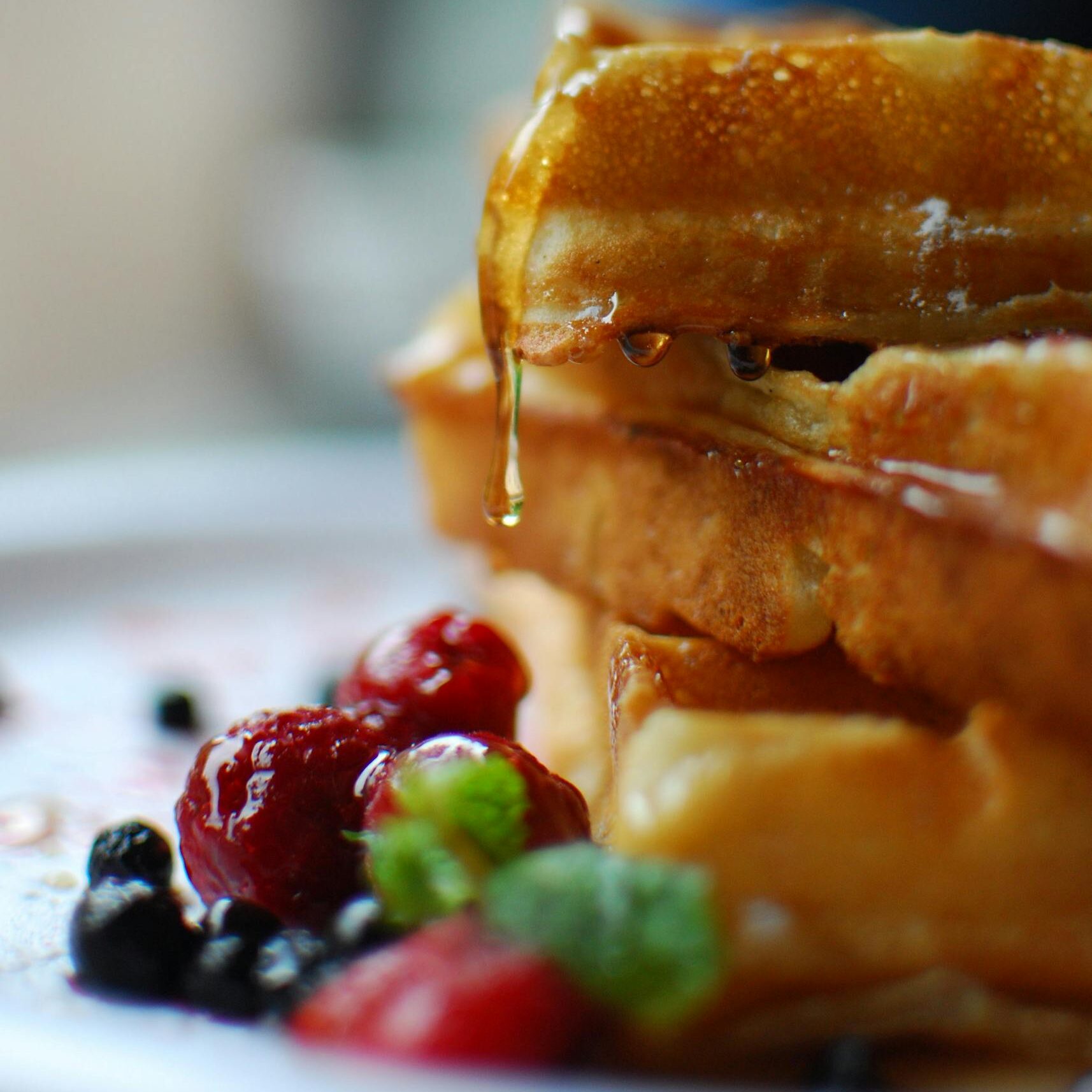 Syrup drips onto stacked waffles with fresh berries, a breakfast delight.