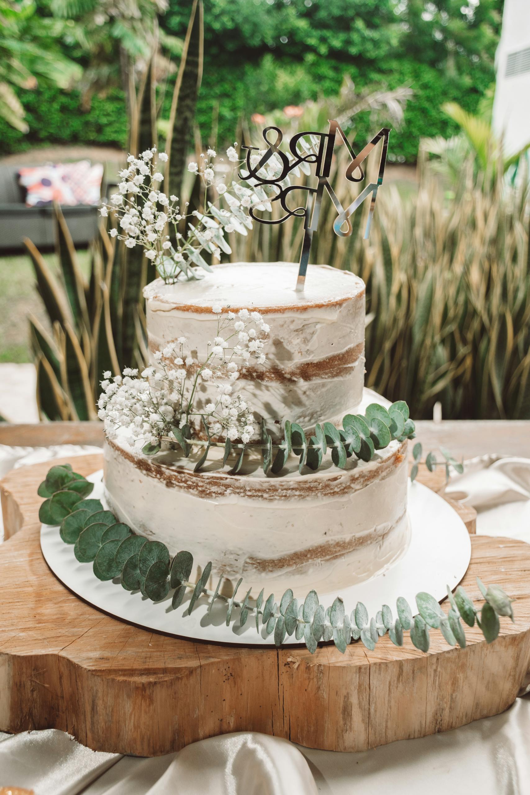 A beautifully crafted rustic wedding cake adorned with greenery and flowers, perfect for outdoor celebrations.