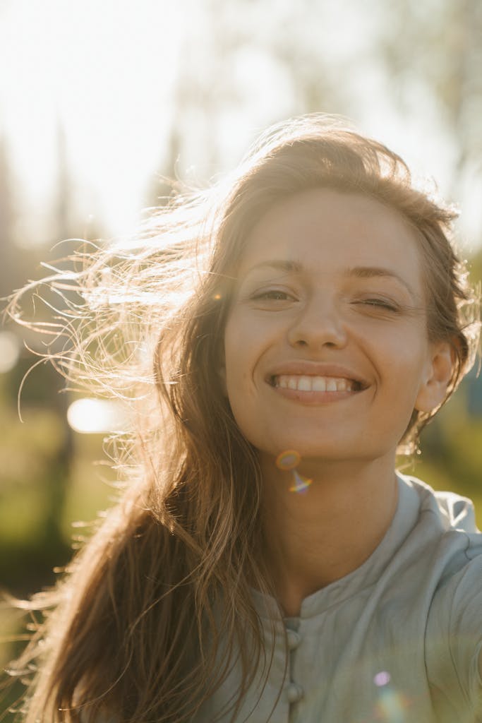 A radiant woman smiling in the sunlight with hair gently blowing outdoors.