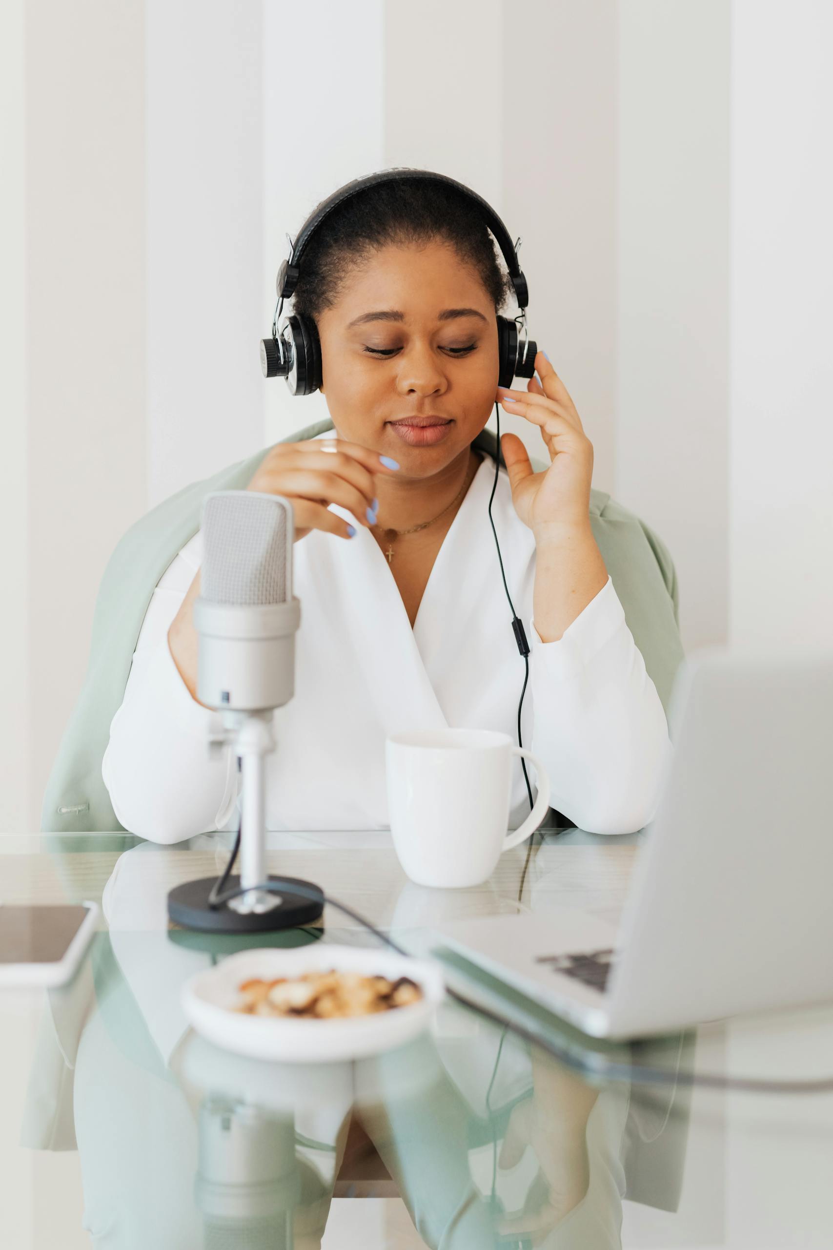 A woman enjoys podcasting at home with a microphone and headphones, embracing technology.