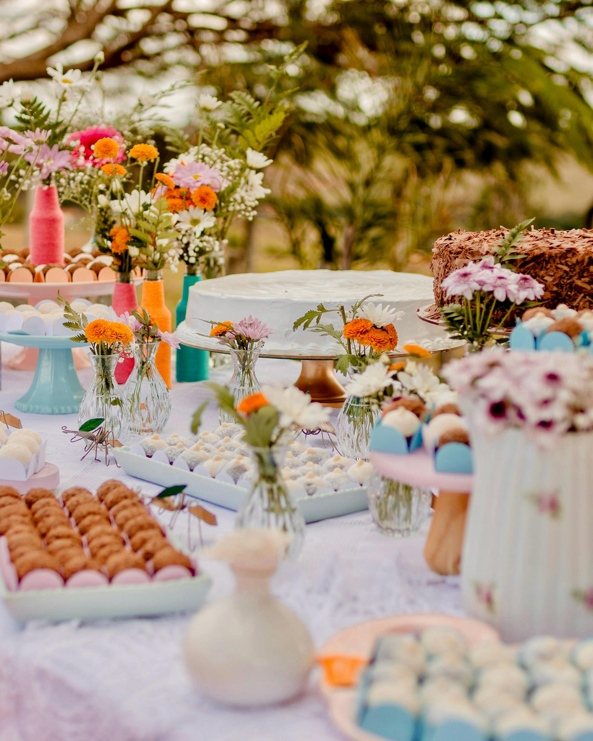 Charming dessert table with sweets and vibrant floral arrangements for outdoor celebration.